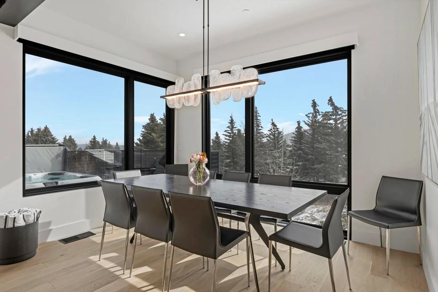 Un comedor moderno tiene una mesa grande junto a ventanas de piso a techo.