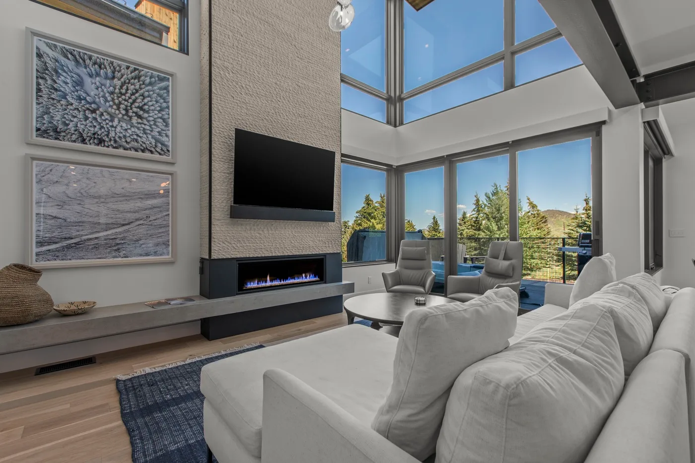 A bright living room with large windows, seating, and a wall-mounted television.