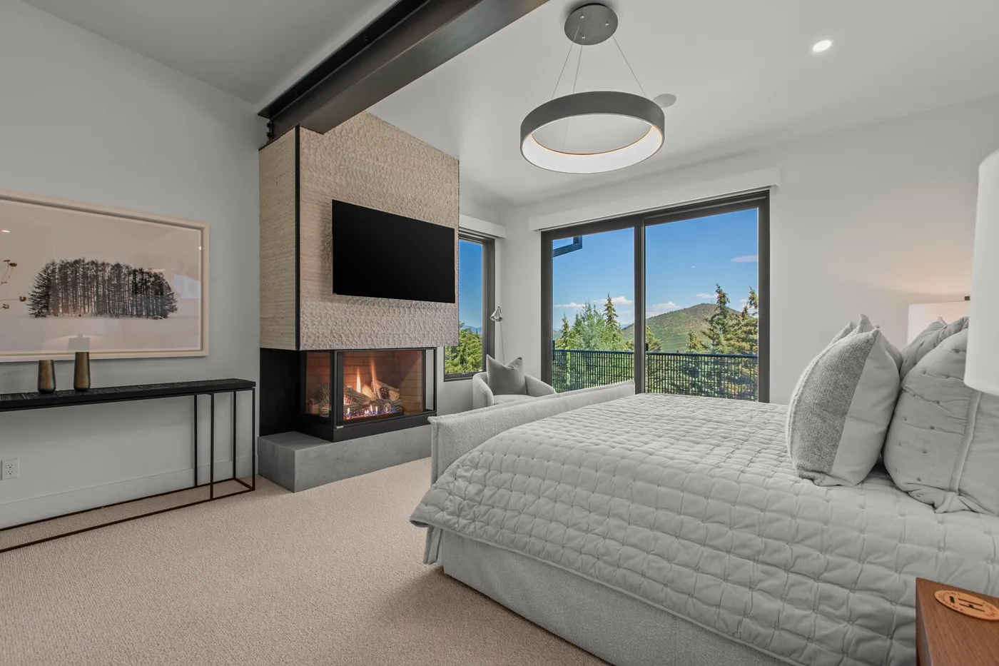 Un dormitorio luminoso con cama, chimenea y grandes ventanales con vistas a la vegetación.