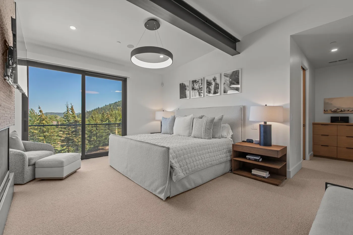 Un dormitorio luminoso con cama, asientos y una gran puerta de vidrio con vistas a la vegetación.