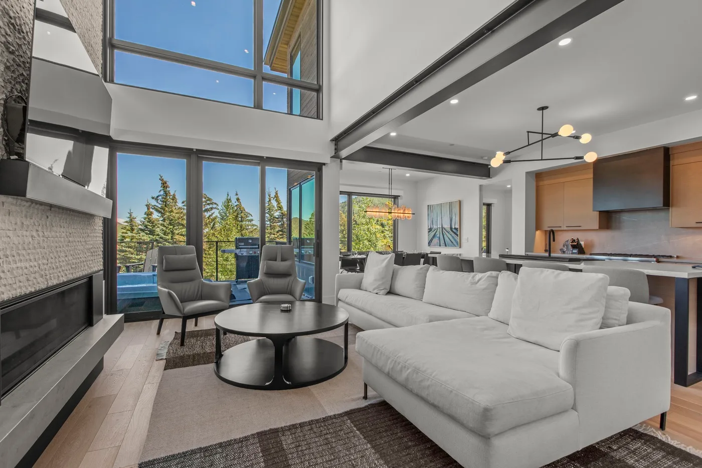 A bright open-plan living room with seating, a fireplace, and large windows.