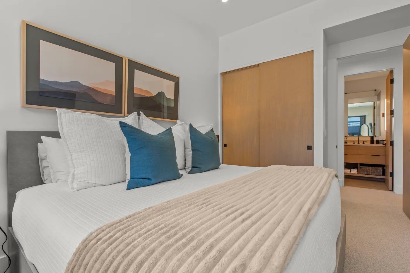 Un dormitorio con una cama bien hecha y cuadros de paisajes enmarcados encima.