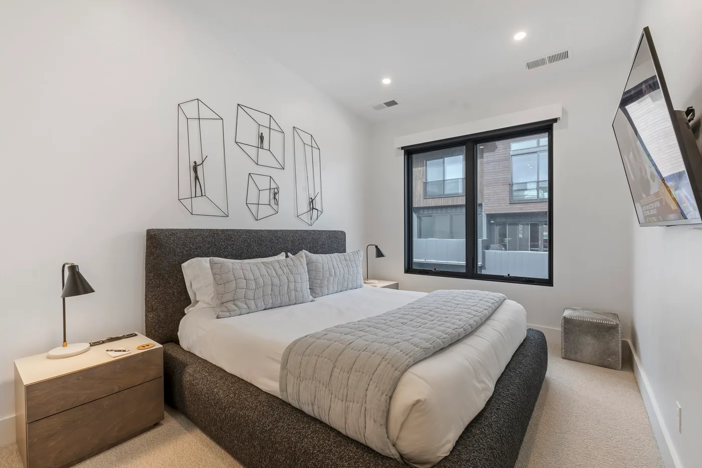 Un dormitorio moderno con una cama bajo arte geométrico y junto a una ventana grande.