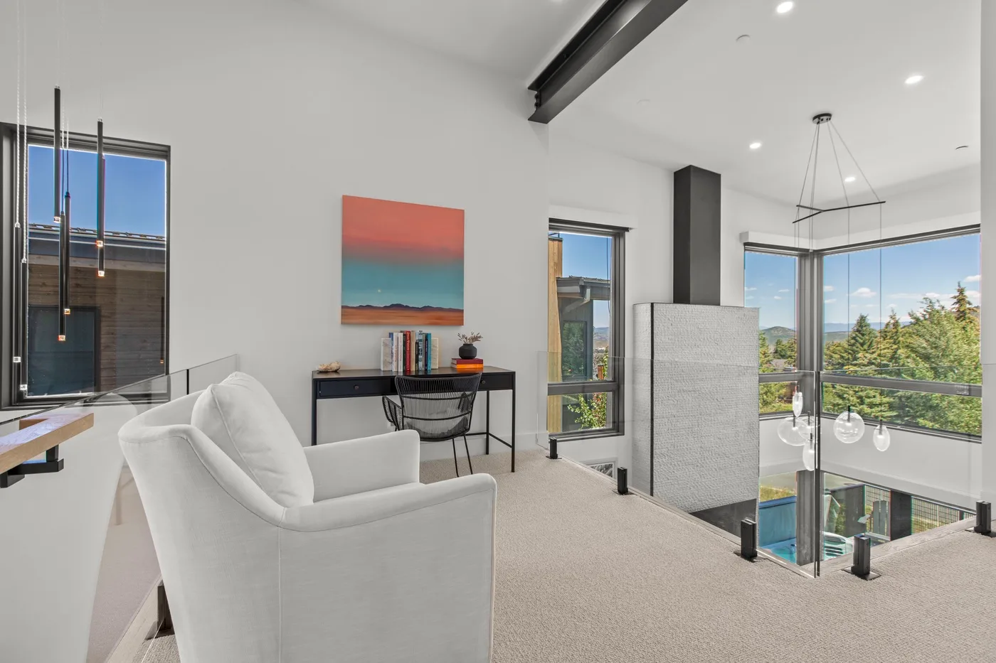 Una luminosa zona de estar tipo loft con un sillón blanco, escritorio y grandes ventanas.