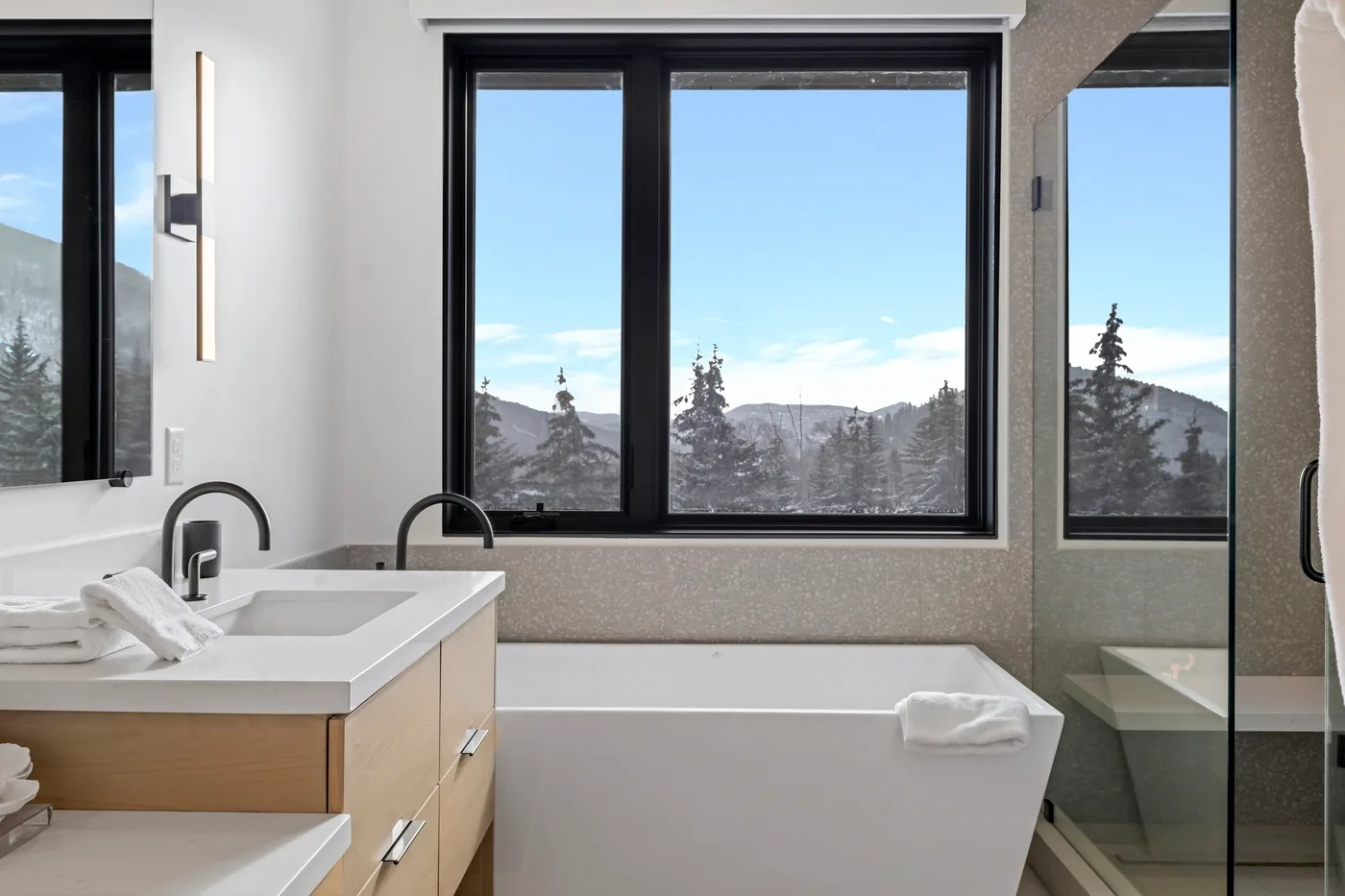 Un baño con bañera, tocador y ventanas con vistas a un paisaje montañoso.