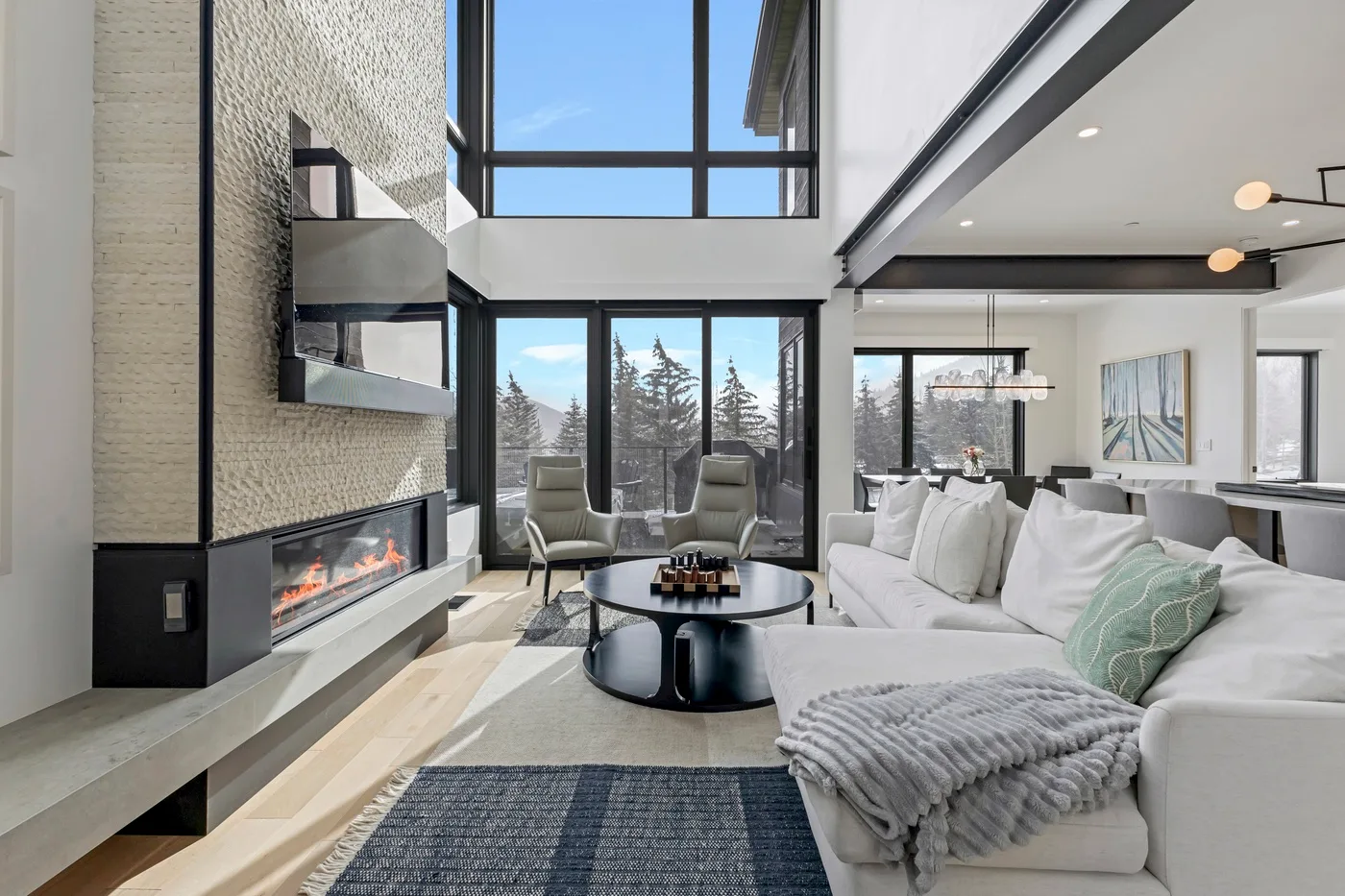 Una sala luminosa con grandes ventanas, una chimenea y asientos alrededor de una mesa baja.