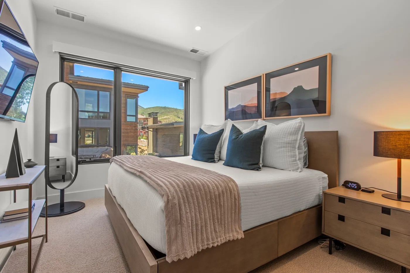 Un dormitorio luminoso con una cama junto a grandes ventanas con vistas a edificios cercanos.