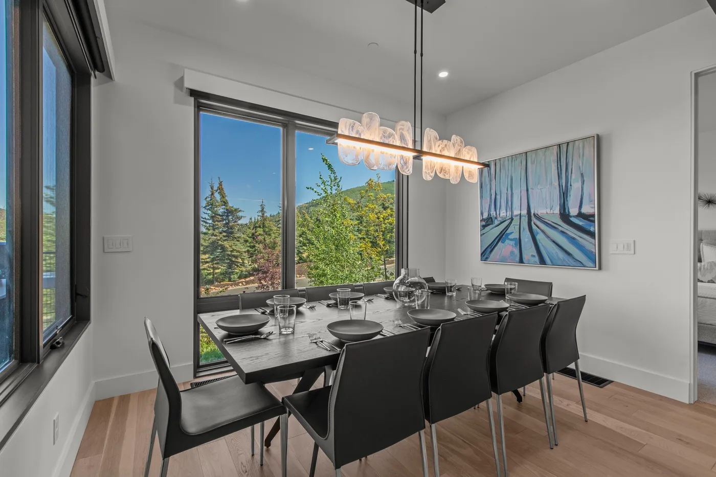 Un comedor moderno con una mesa larga, asientos oscuros y grandes ventanas.