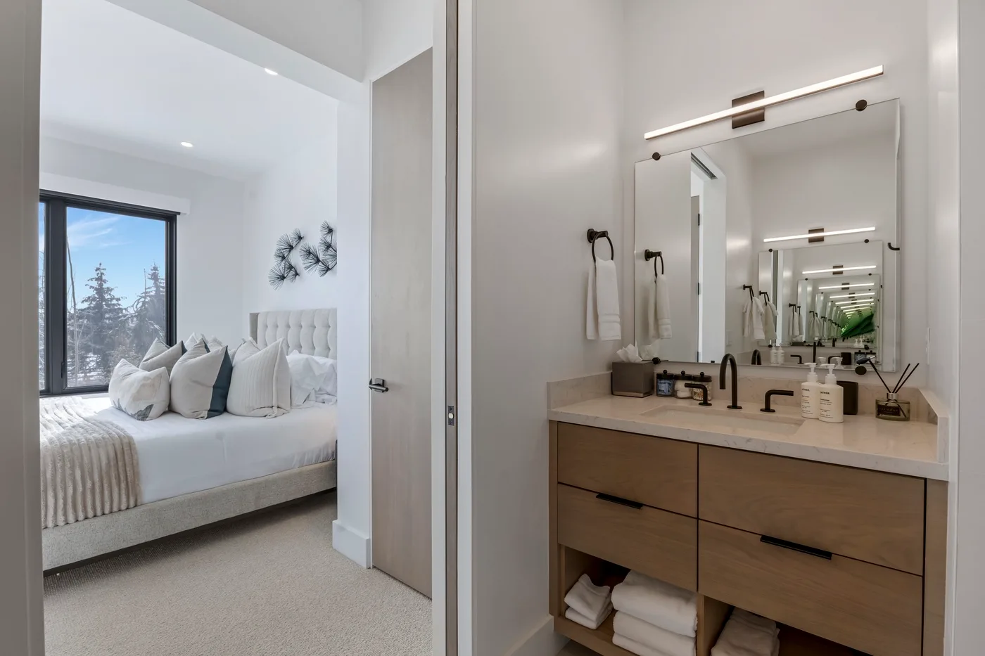 Un dormitorio luminoso con una cama junto a un tocador de baño y un espejo.