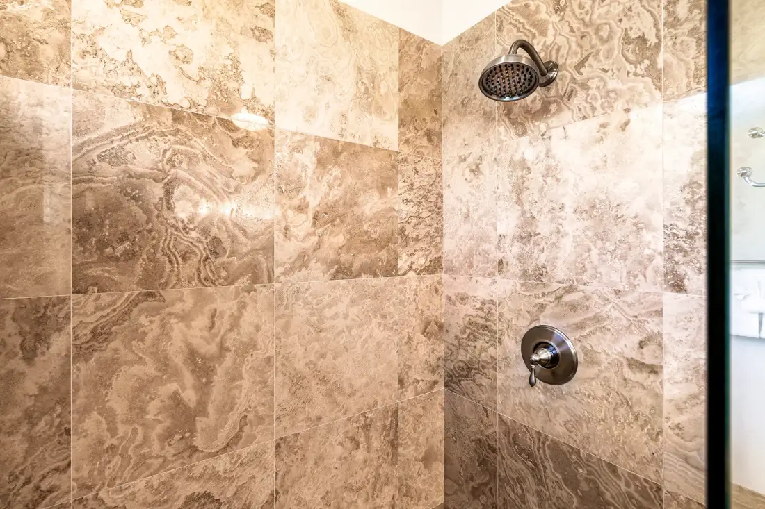 Una ducha con azulejos, alcachofa de pared y control.