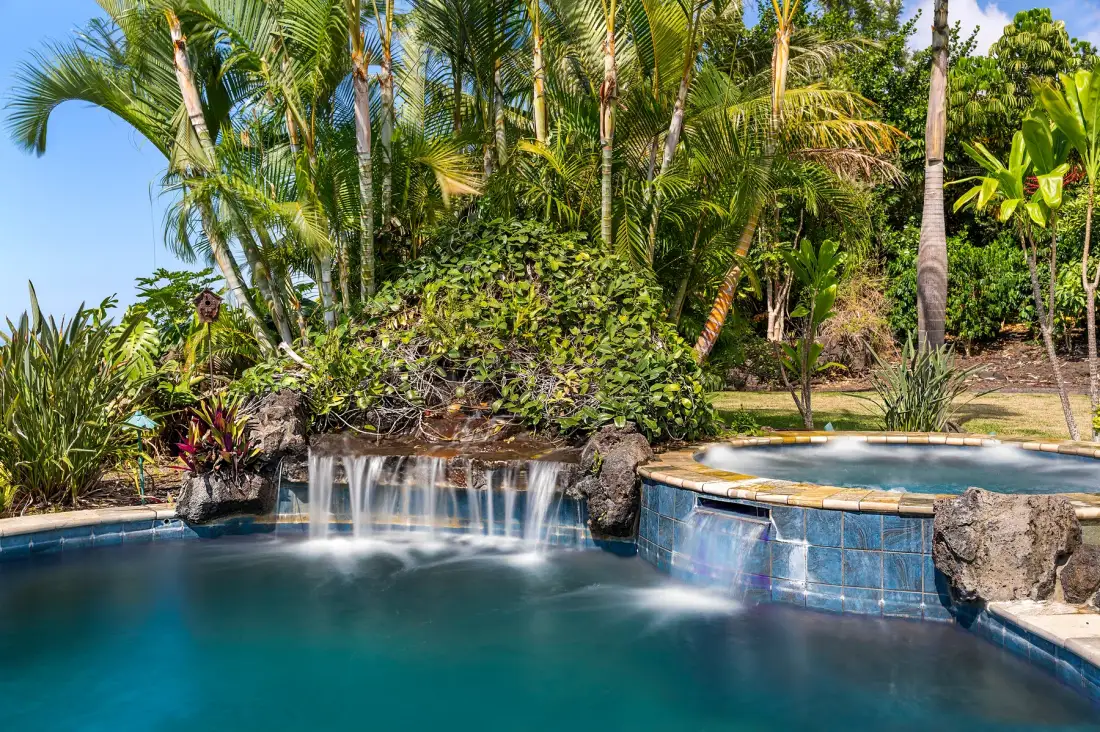 Una piscina tropical con una pequeña cascada y exuberantes palmeras.