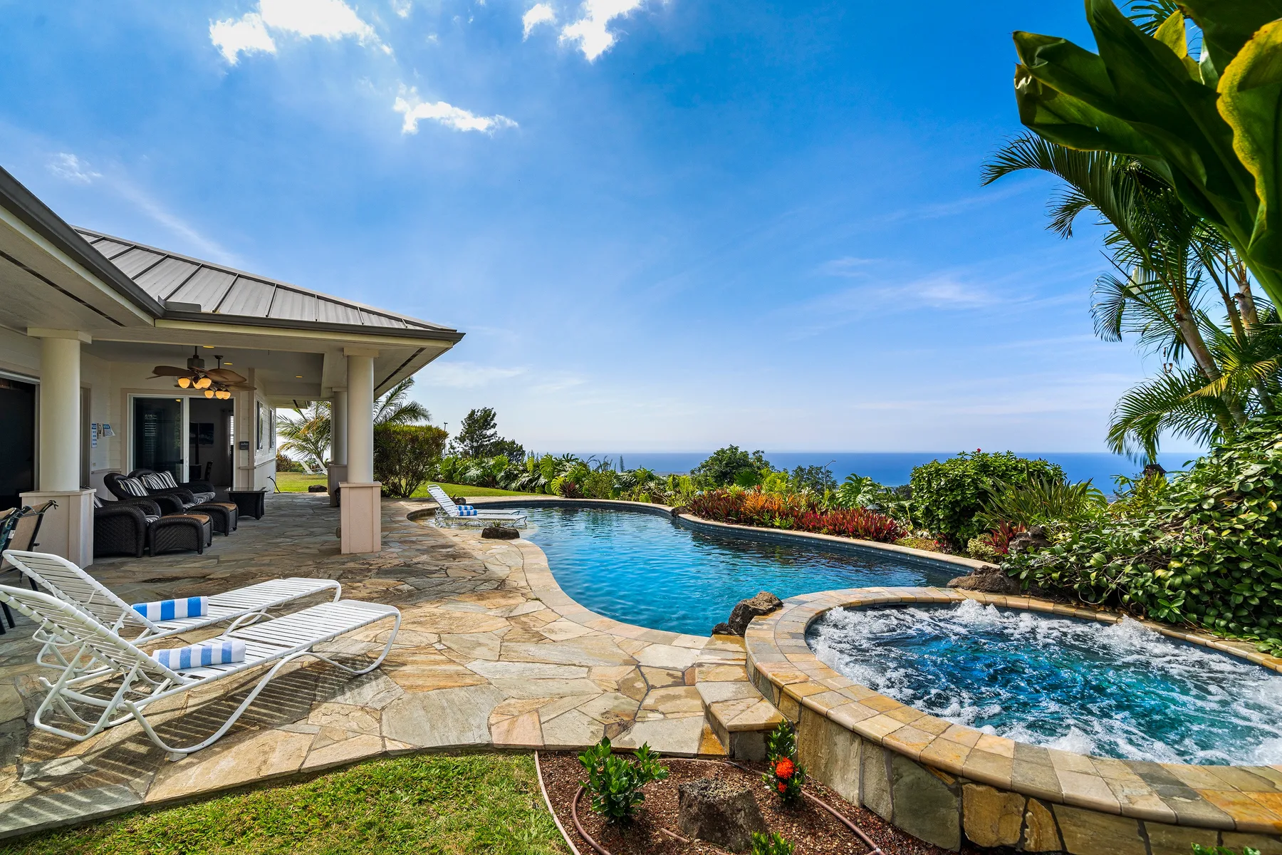 Una piscina exterior y un jacuzzi contiguo están junto a un patio cubierto con vistas al océano.