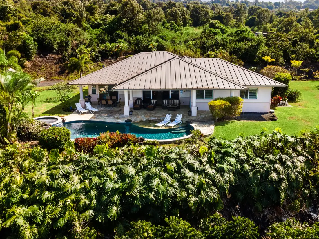Una casa baja da a una piscina curva rodeada de vegetación frondosa.