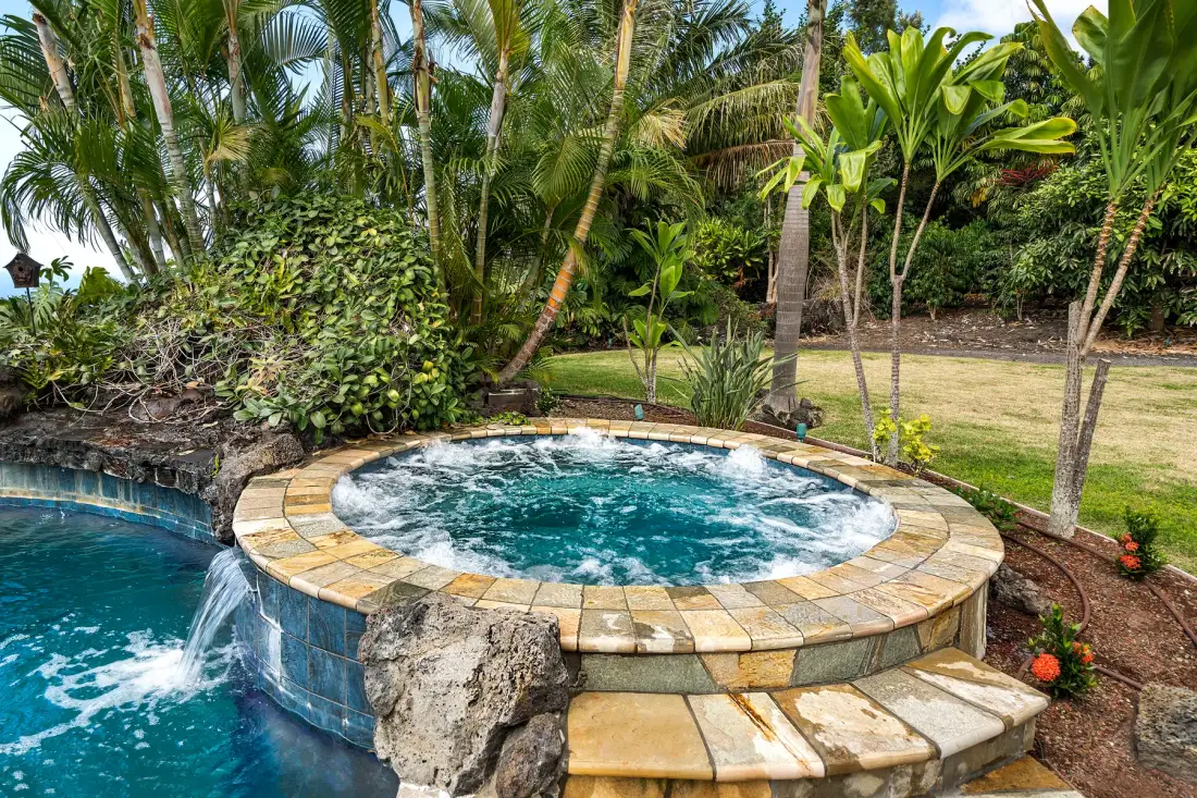 Una piscina circular con burbujas está junto a una piscina más grande en un jardín tropical.