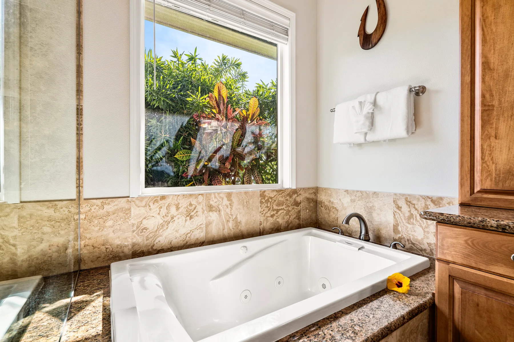 Un baño con una bañera blanca bajo una ventana que da a vegetación tropical.