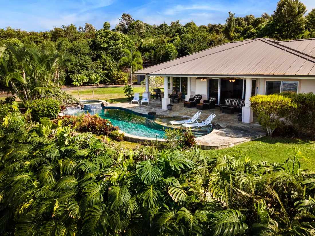Una casa y una piscina al aire libre están rodeadas de abundante vegetación tropical.