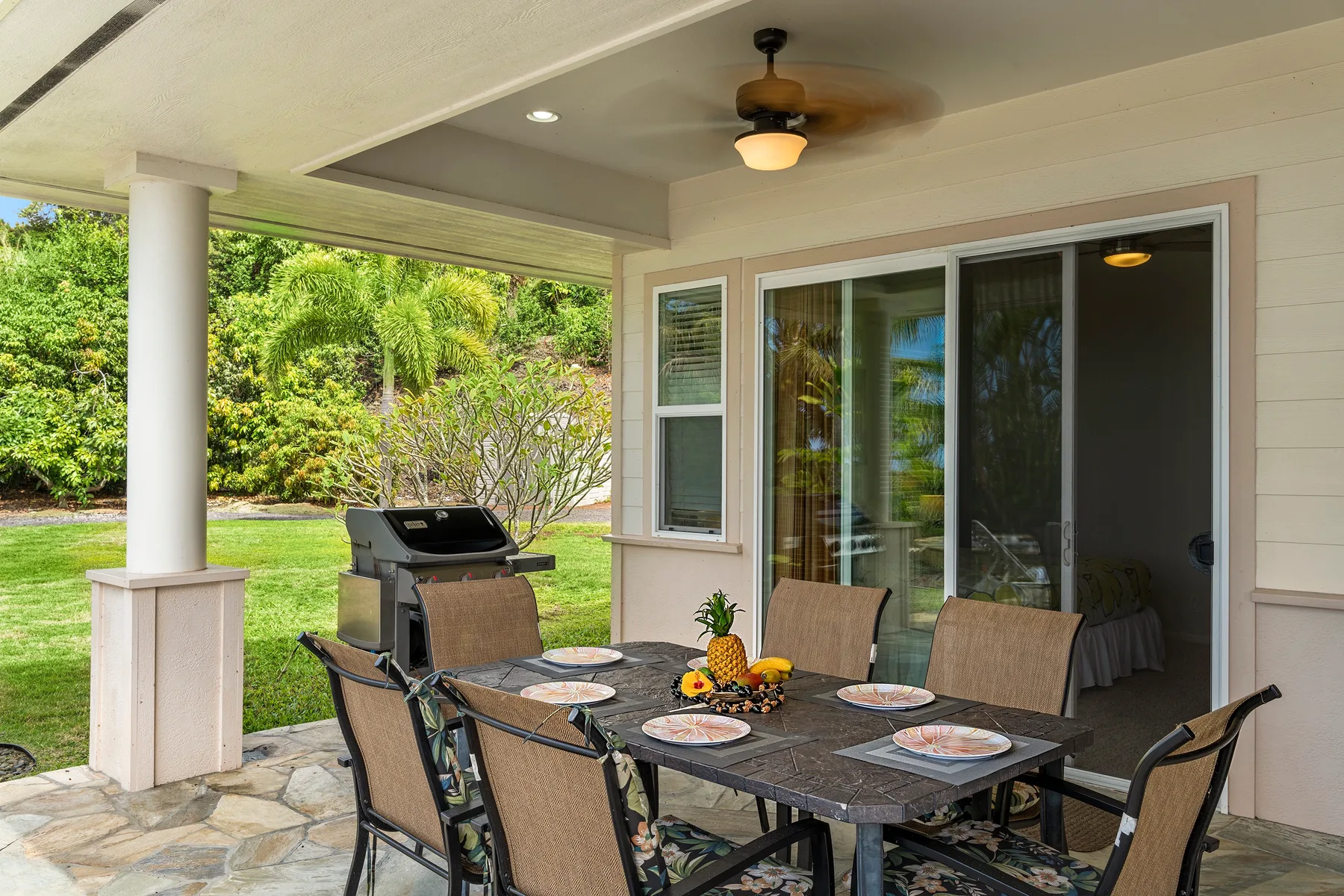 Un comedor exterior cubierto da a un jardín, con una mesa y asientos.