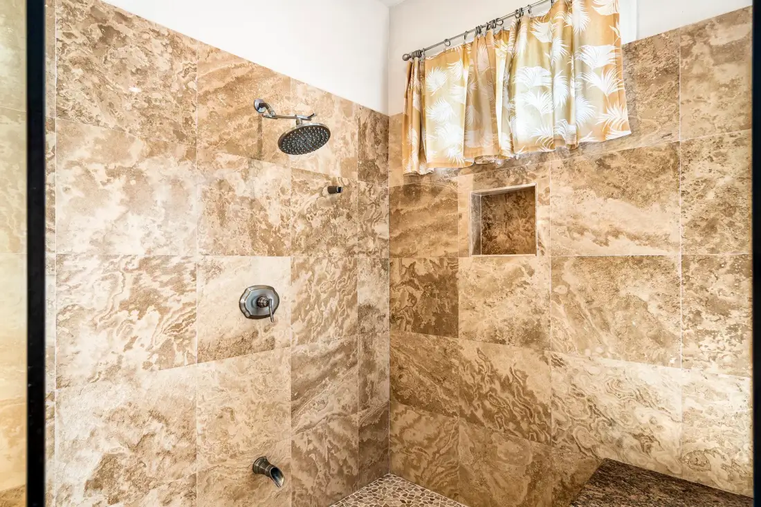Una zona de ducha alicatada con un cabezal de ducha y una ventana con cortina.
