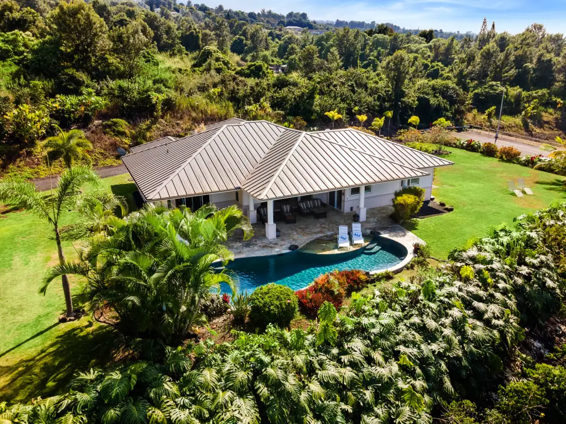 Una casa con una piscina curva se encuentra entre jardines y árboles.