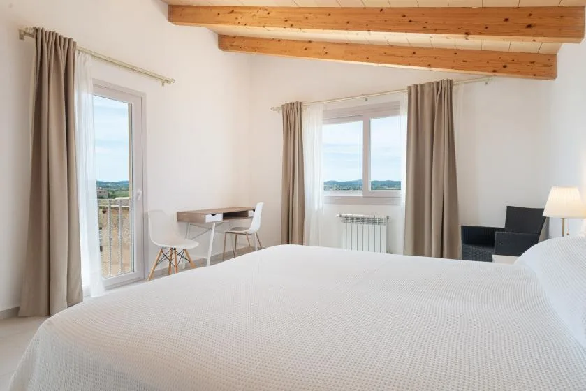 Un dormitorio luminoso con una cama, un escritorio pequeño y ventanas con vistas al agua.