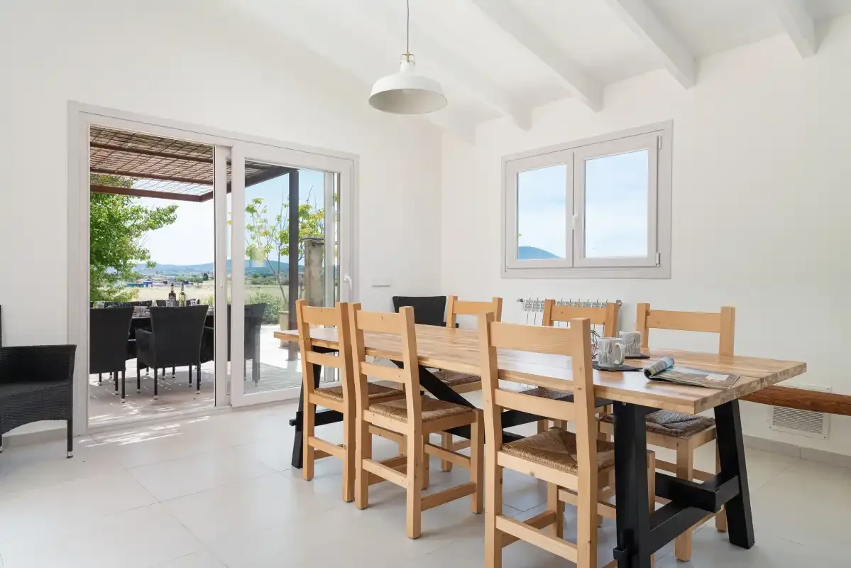 Un comedor luminoso con una mesa larga de madera junto a ventanas y puertas corredizas de vidrio.