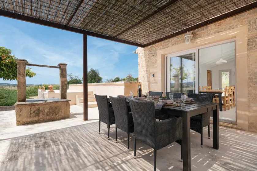 Comedor exterior cubierto con una mesa y asientos junto a puertas de vidrio.