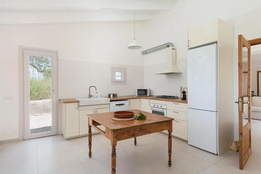 Una cocina luminosa con gabinetes blancos y una mesa de madera en el centro.