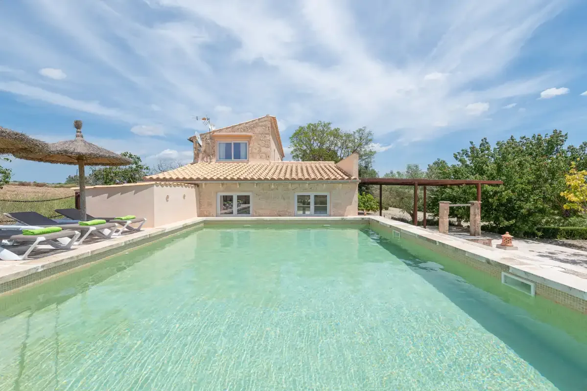Una piscina al aire libre está junto a una casa baja y un patio con sombra.