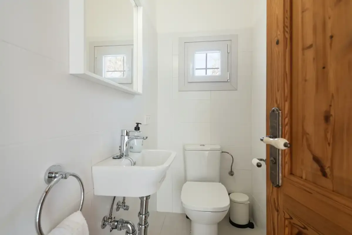 Un baño pequeño con lavabo de pared, inodoro y puerta de madera.