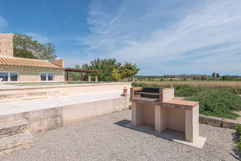 Un patio exterior pavimentado con una parrilla empotrada junto a un edificio bajo.