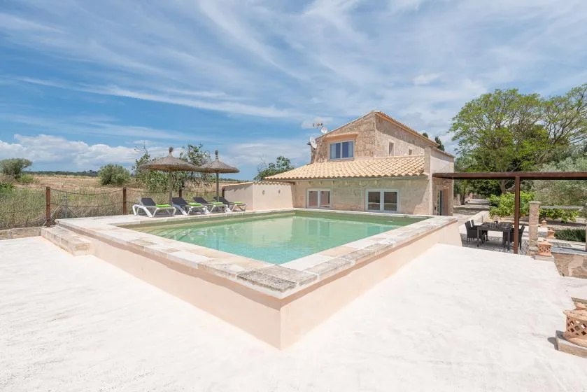 An outdoor swimming pool sits beside a stone house on a sunny patio.
