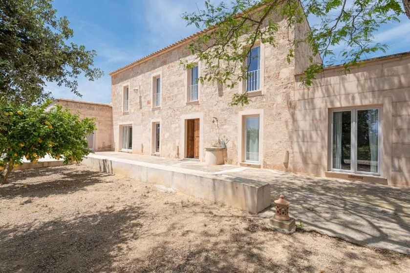 Una casa de piedra se encuentra junto a un patio exterior sombreado por árboles.