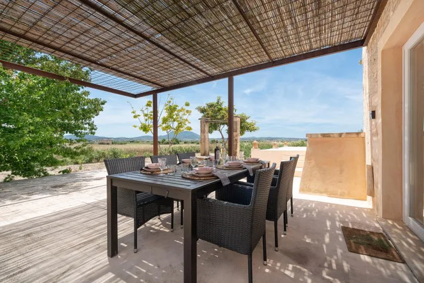 Comedor exterior bajo una pérgola sombreada, con una mesa y asientos.