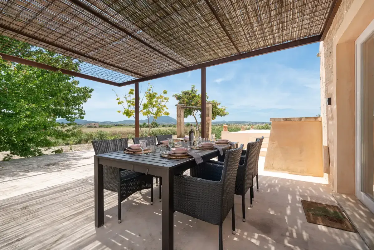 Una zona de comedor exterior sombreada tiene una mesa y asientos junto a un paisaje abierto.