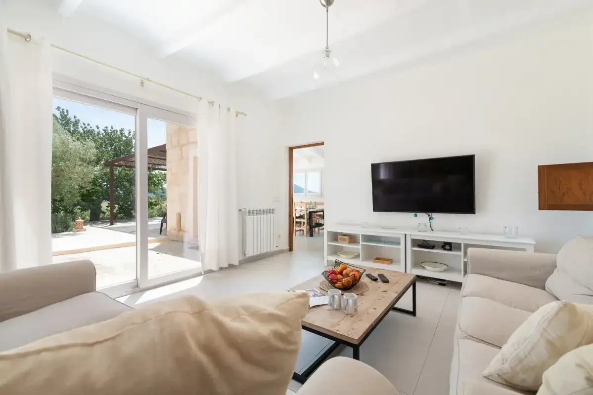 Una sala de estar luminosa con asientos, un televisor y puertas corredizas de vidrio hacia un patio.