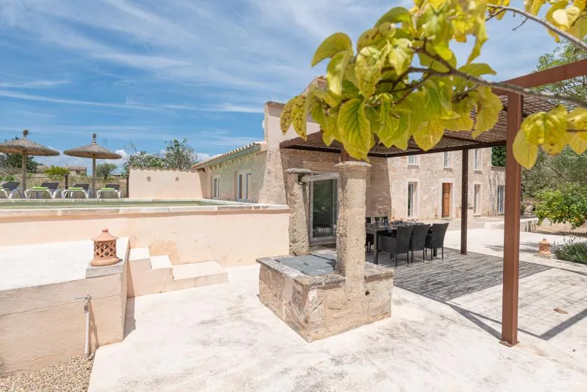 Un patio exterior de piedra con pérgola y mesa de comedor junto a un muro bajo.