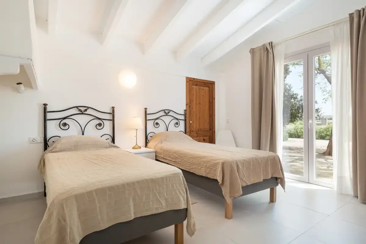 Un dormitorio luminoso con dos camas y puertas de cristal que dan a un patio.
