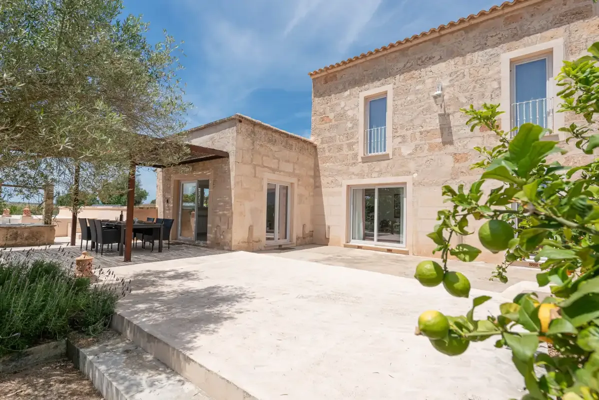 Una casa de piedra da a un patio soleado con muebles de comedor al aire libre.