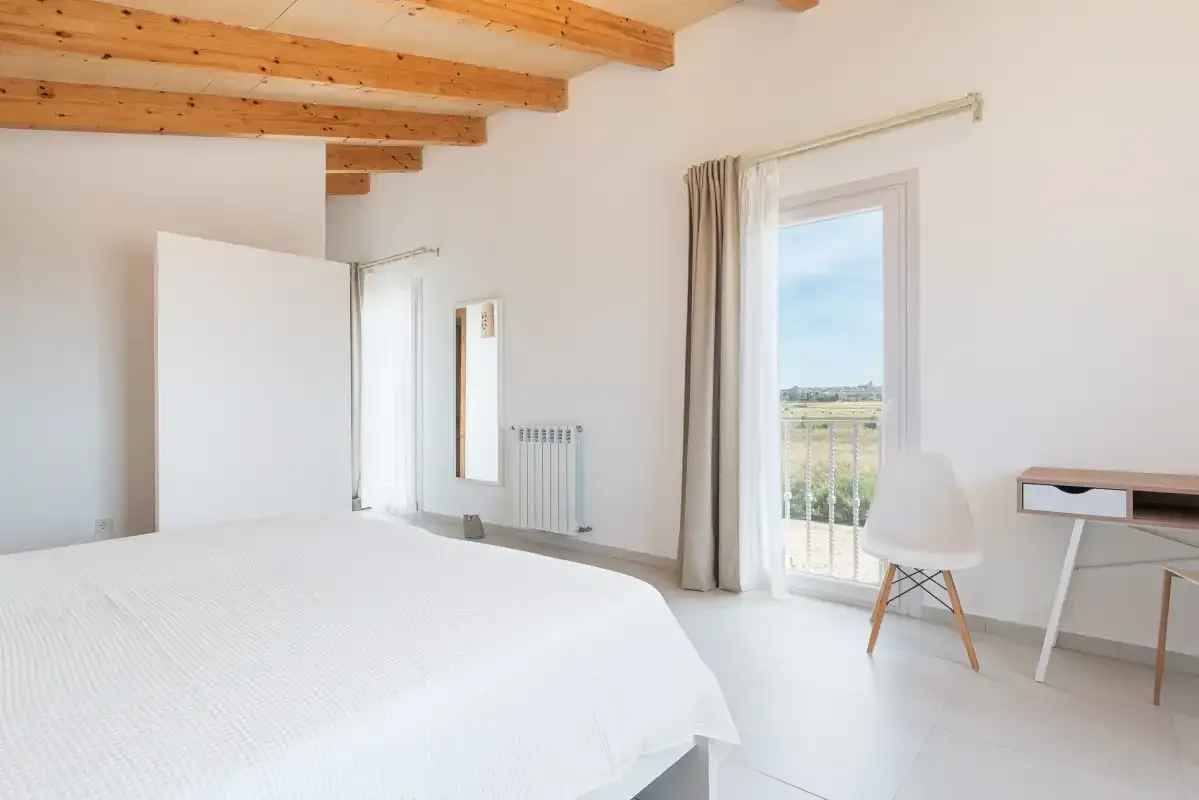 Un dormitorio luminoso con una cama, vigas de madera vistas y una ventana.