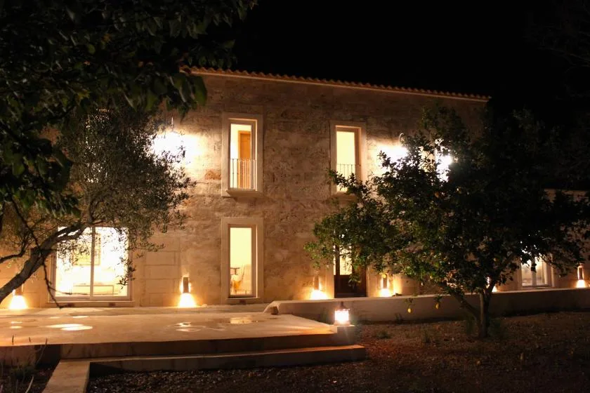 Un edificio de piedra de noche, con ventanas iluminadas y árboles delante.