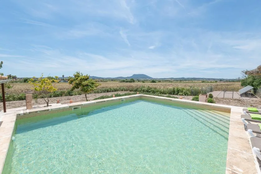 An outdoor swimming pool overlooks open fields beneath a blue sky.