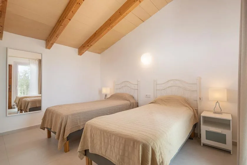 Un dormitorio luminoso con dos camas y vigas de madera a la vista en el techo.