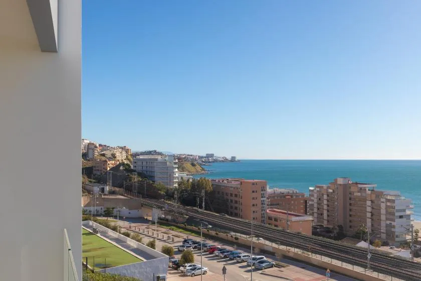 Una ciudad costera y el mar azul se ven más allá de las vías y la carretera.