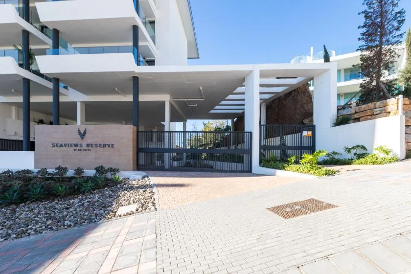 Entrada de un edificio moderno con acceso cerrado y jardines junto a la entrada.