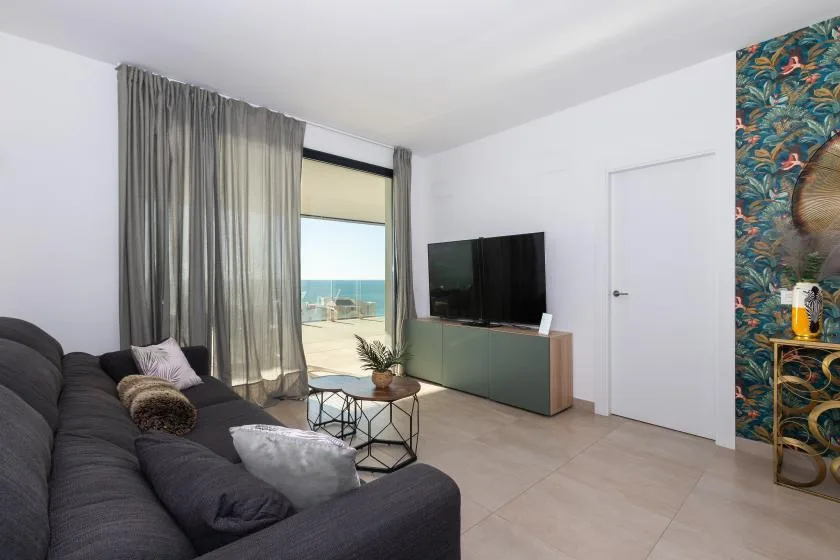 Una sala de estar con un sofá oscuro, un televisor y vistas al mar.