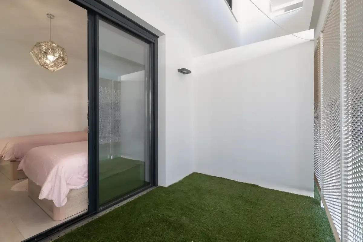 Un pequeño patio exterior con suelo verde junto a un dormitorio con una cama.