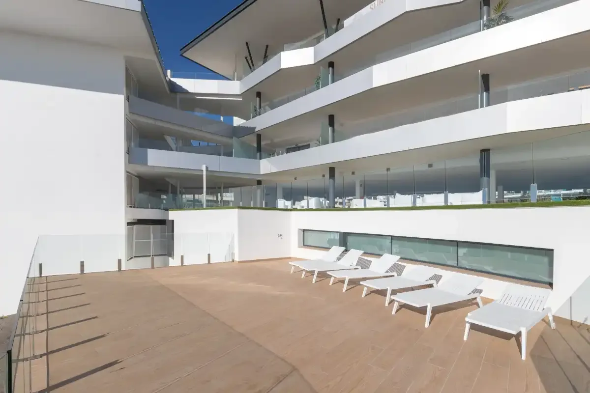 Una terraza de patio moderna con asientos blancos y balcones con frentes de vidrio.
