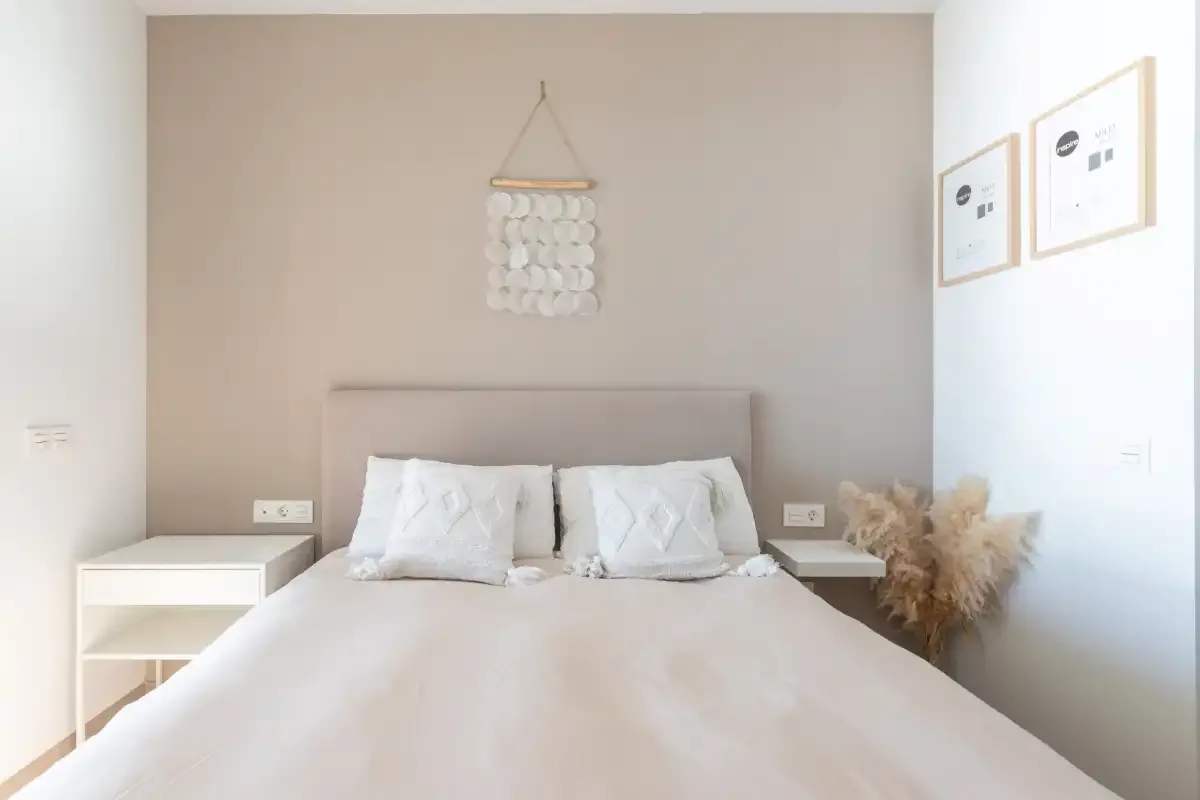 Un dormitorio con una cama bien tendida y dos láminas en la pared.