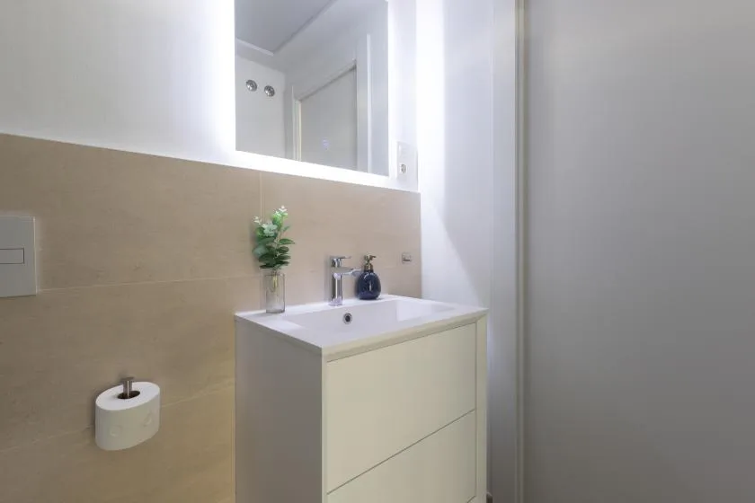 Un lavabo de baño con espejo frente a una pared alicatada.