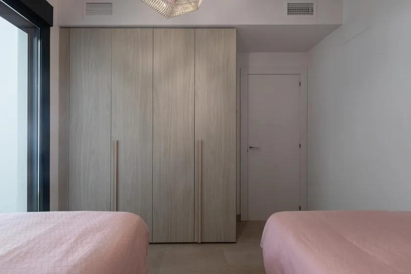 Un dormitorio con un armario de madera clara y ropa de cama rosa.